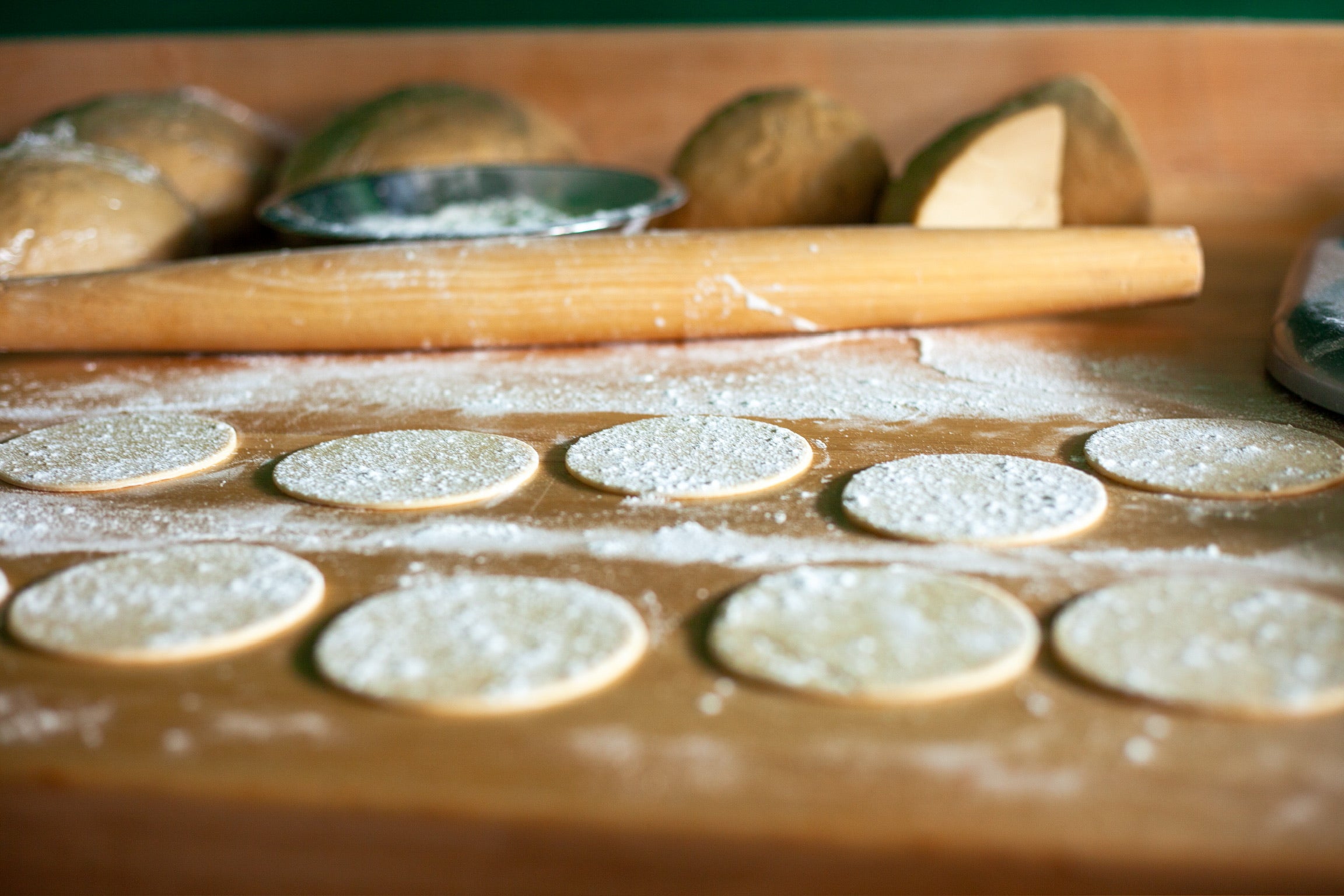 Cannoli shells being rolled with a rolling pin in the background of the photo